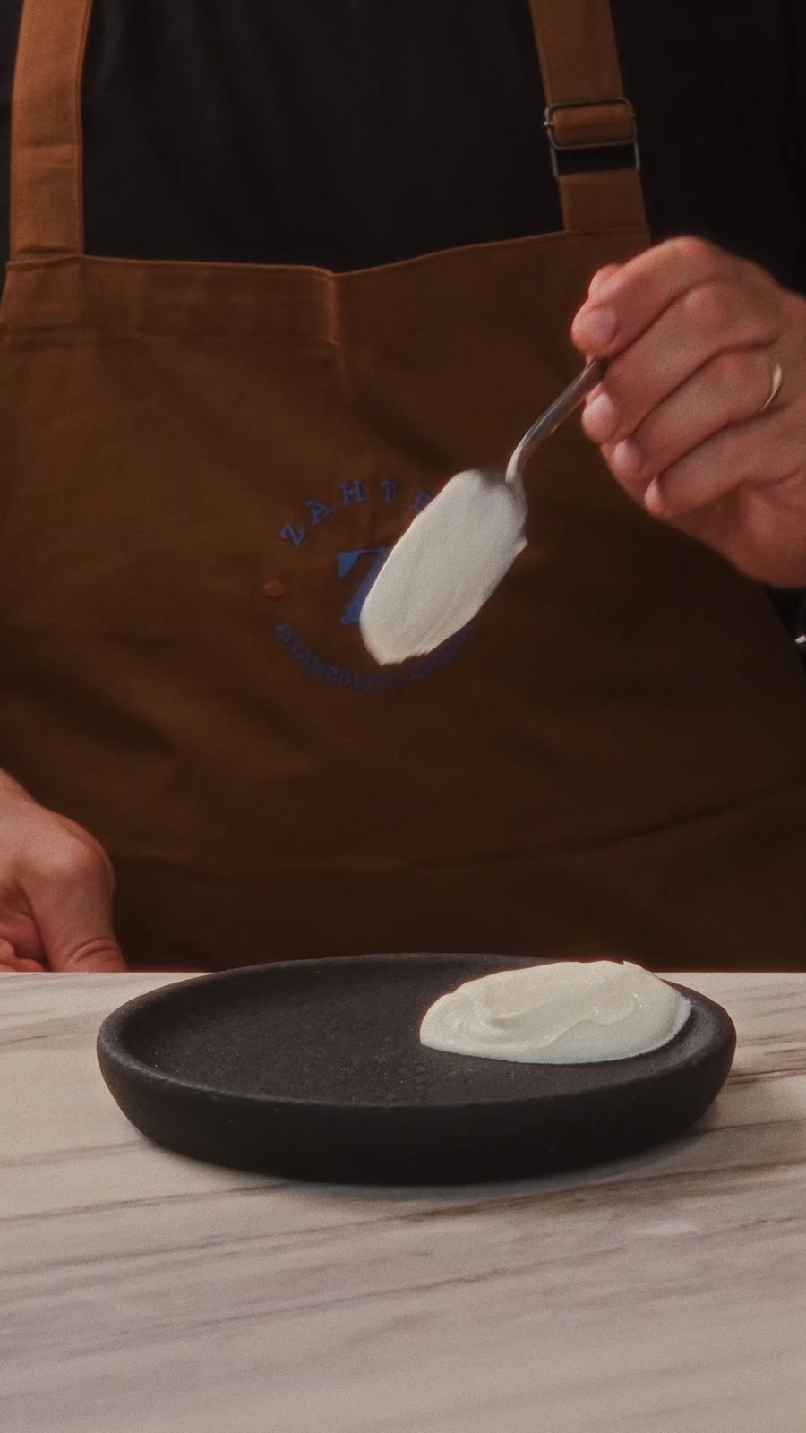 A chef in a Zahter apron plating yoghurt